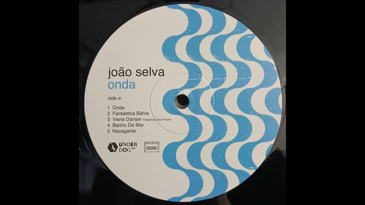 Load video: Joao Selva - Onda, LP on the turn table. Black vinyl. Label is white, with the writing on the left half, blue lines (stylised waves) on the right half. The turn table is a Technics SL1200 MK3 with a green metal cover.